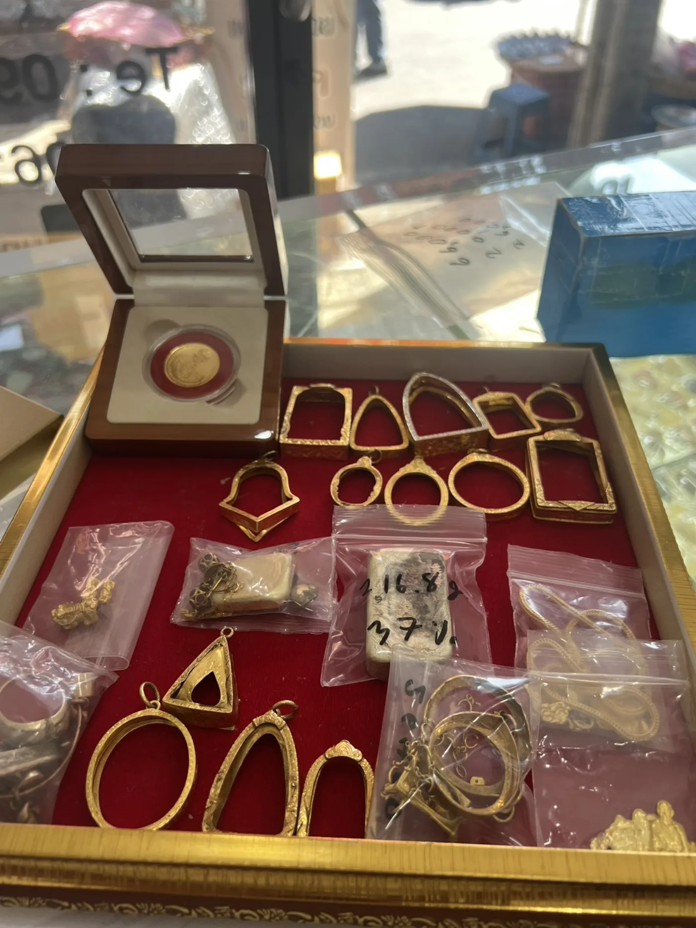 เหรียญทองในกล่องใบรับรองวางคู่กับกรอบพระทองบนถาดแดง